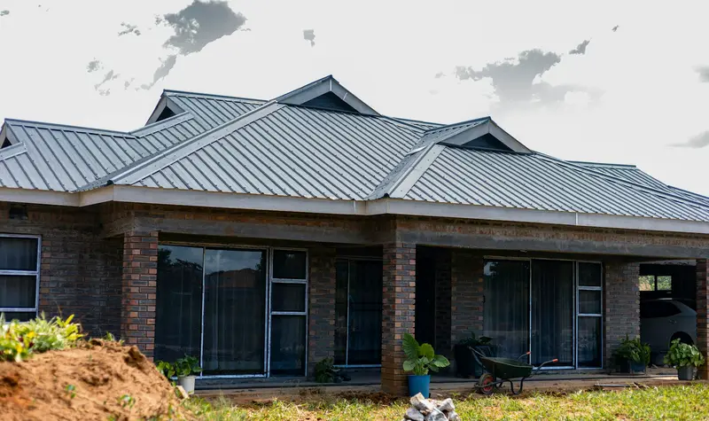 A brick bungalow with a grey iron-sheet roof and a freshly dug garden